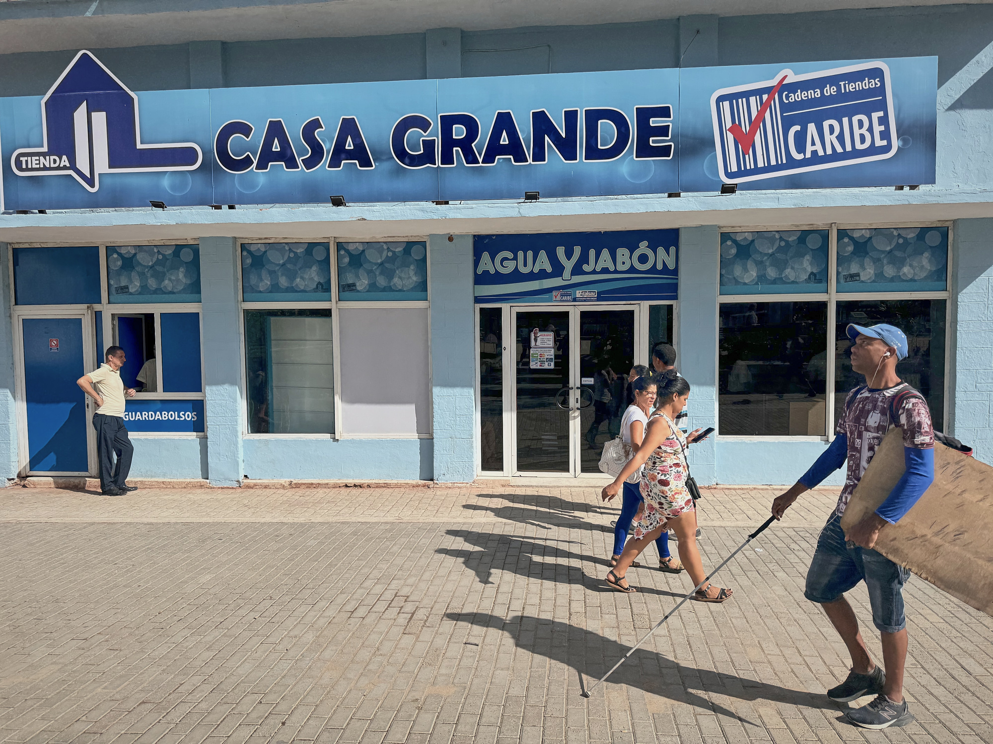 Outside Casa Grande, an MLC (dollar-based) store in Havana, shoppers pass beneath a spotless blue façade. The contrast with nearby CUP-only shops is stark, this one trades in U.S. currency, not pesos.