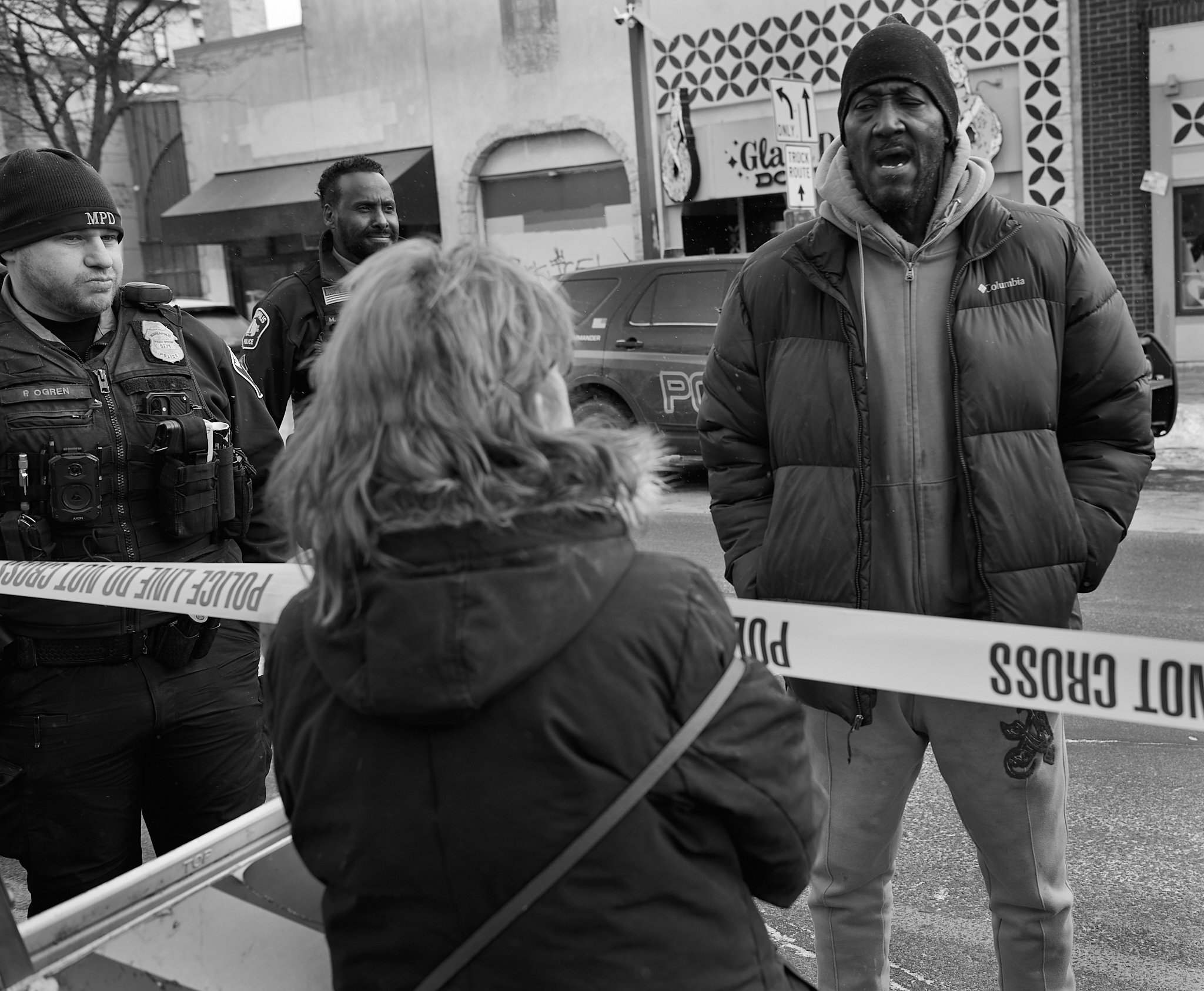 A man speaks across police tape during a confrontation, saying the killing reflects what he described as a common experience in Black America and warning that injustice can happen to anyone, as police stand guard.