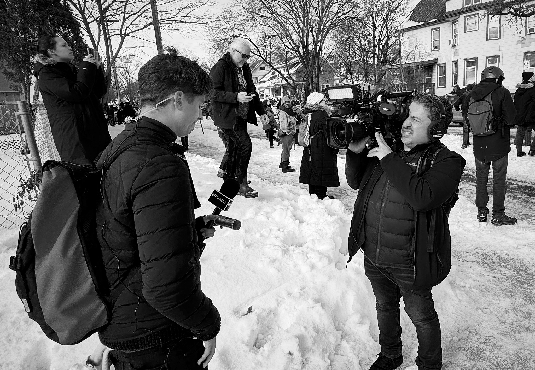A national correspondent films a live report while bystanders gather nearby following the fatal shooting of a woman by an ICE agent in Minneapolis. The moment captures the strain of reporting as events continued to evolve on the ground.
