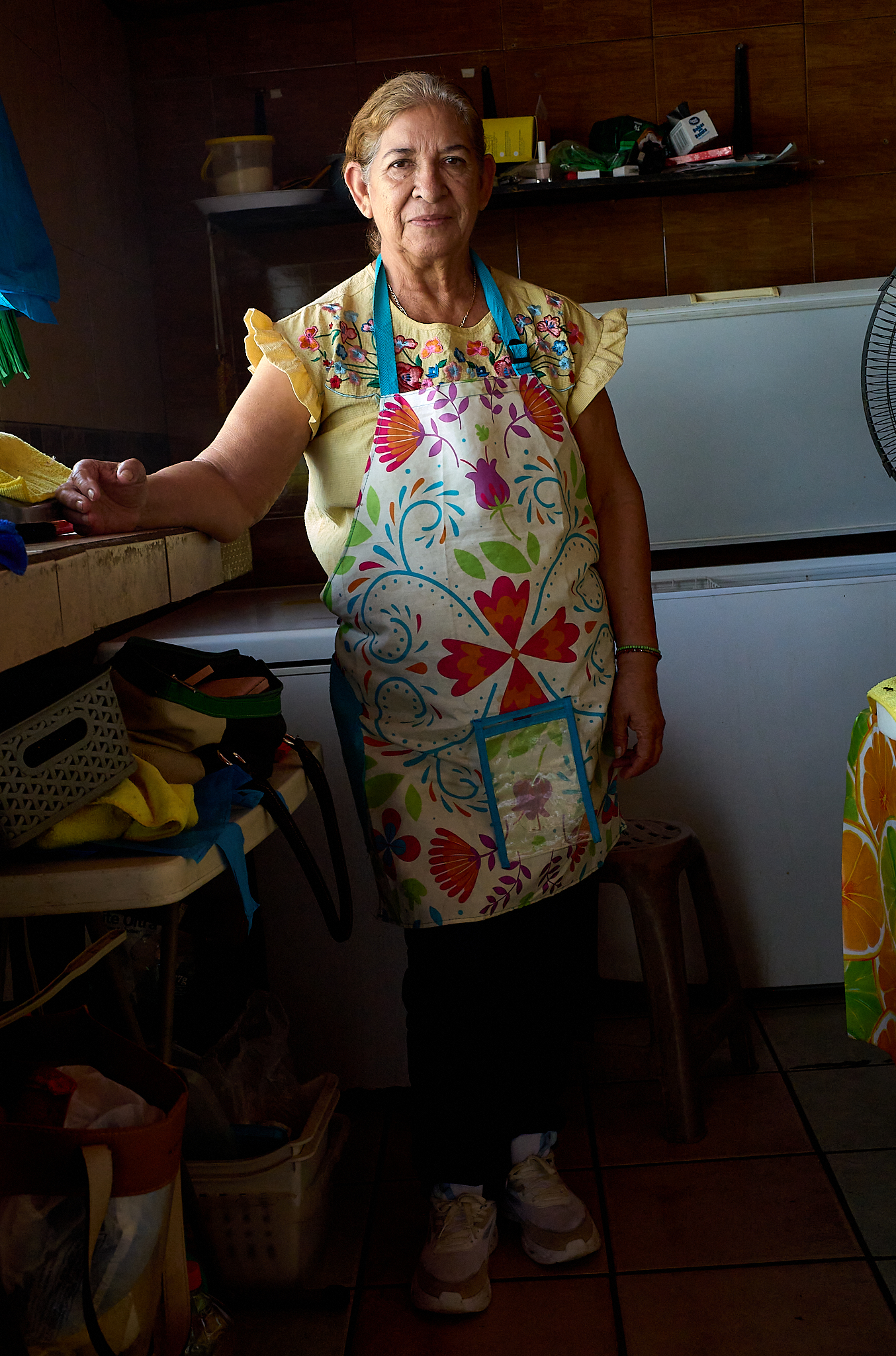 A woman stands inside a small home kitchen in Cabo San Lucas, where she prepares and sells meals to neighbors. Informal, home-based kitchens like this are common in the area.