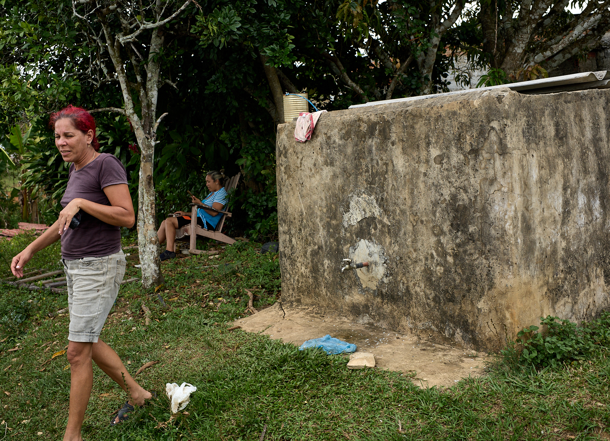 Sisleidi walks past the family’s outdoor gray-water tank. During the dry months, water for bathing and cleaning is trucked in and stored here, while drinking water continues to come from a spring higher in the hills.