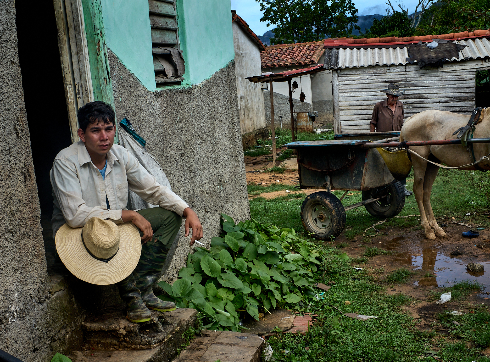 Michael rests on the back stoop after tending the family’s yuca plants. His grandfather, Miguel, moves in the background—a quiet moment in the daily rhythm of life on their multigenerational farm in Viñales.