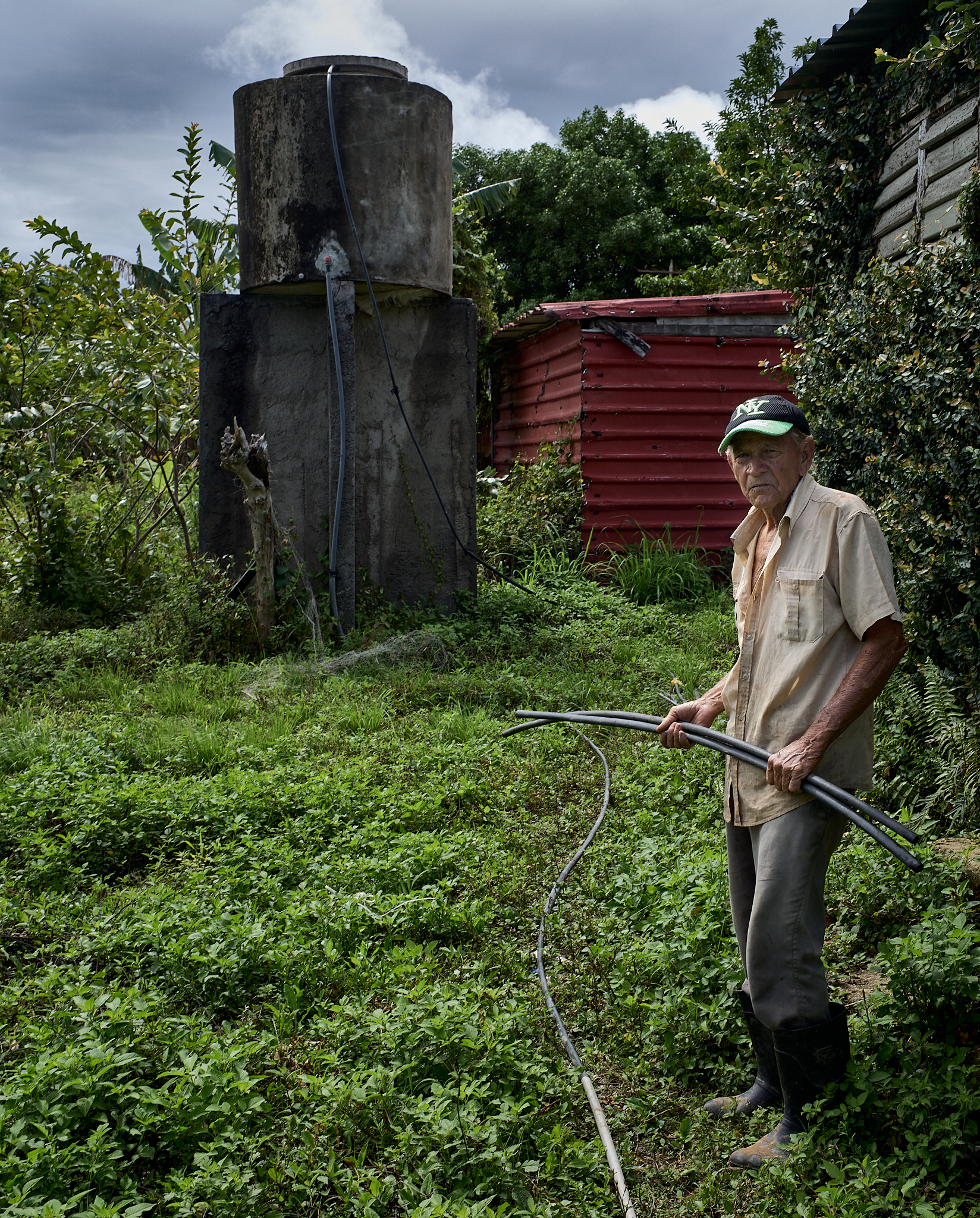 A neighbor repairs a gravity-fed water line running from the natural spring in the hills above the village. In the background sits one of the gray-water tanks used during the dry season when additional water must be trucked in.