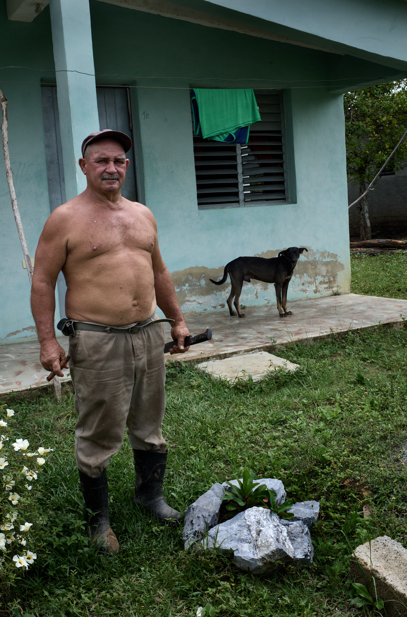 Just down the path from Michel's home, a neighbor pauses outside his house with a machete in one hand and a cigar in the other. In Viñales, both are common tools—one for cutting brush, the other for taking a break.